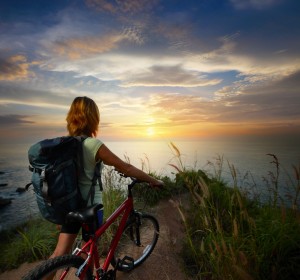 Ban med cykel ser ud over solnedgang foran havet