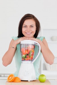 Kvinde i køkkenet med blender fuld af grøntsager og frugt