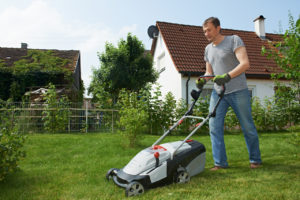 Mand slår sin græsplæne med en græsslåmaskine
