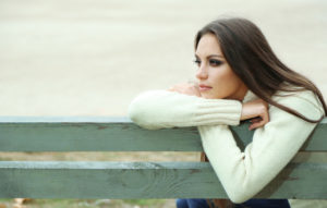 Ung kvinde sidder alene på en bænk og ser tænksom ud