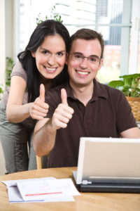 smilende ungt par giver thumbs up foran computer