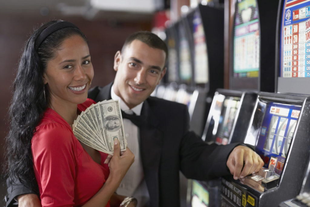 ungt par med pengesedler foran spillemaskine på casino